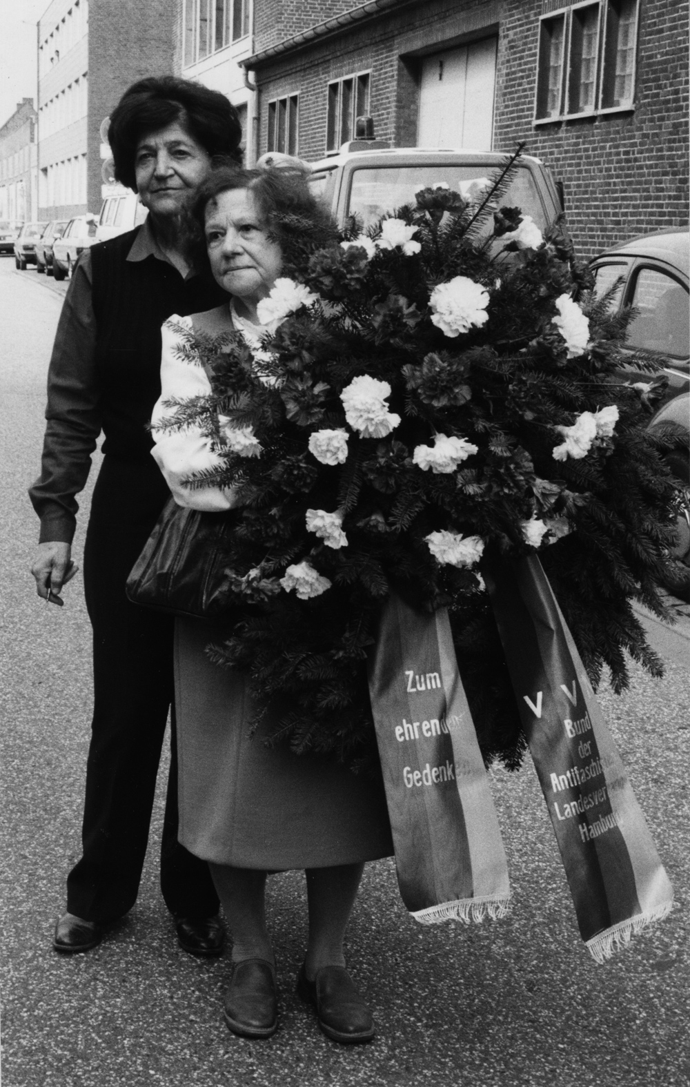 Zwei Frauen mit einem großen Blumengedenkkranz